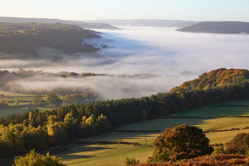 Curbar cloud inversion This landscape photograph captures a morning view of a cloud-inversion over Curbar Edge in the Peak District, Derbyshire, United Kingdom. Taken at sunrise during autumn, the image showcases mist and low clouds enveloping the rural valley below, with layers of trees displaying seasonal colours typical of nature in October. The cloud-inversion effect is prominent above the rolling hills and fields, highlighting Curbar Edge as a recognizable landmark in the area. The interplay between sunlight and mist emphasizes the tranquil beauty of the rural Peak District landscape in autumn.